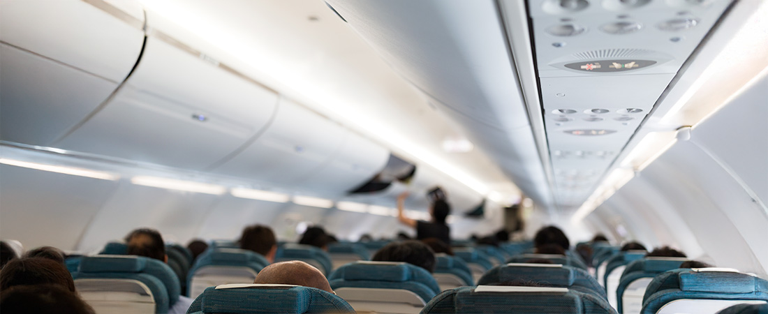 ista interior del pasillo de una cabina de avión vacía, mostrando las filas de asientos, los compartimentos superiores y la iluminación del techo.