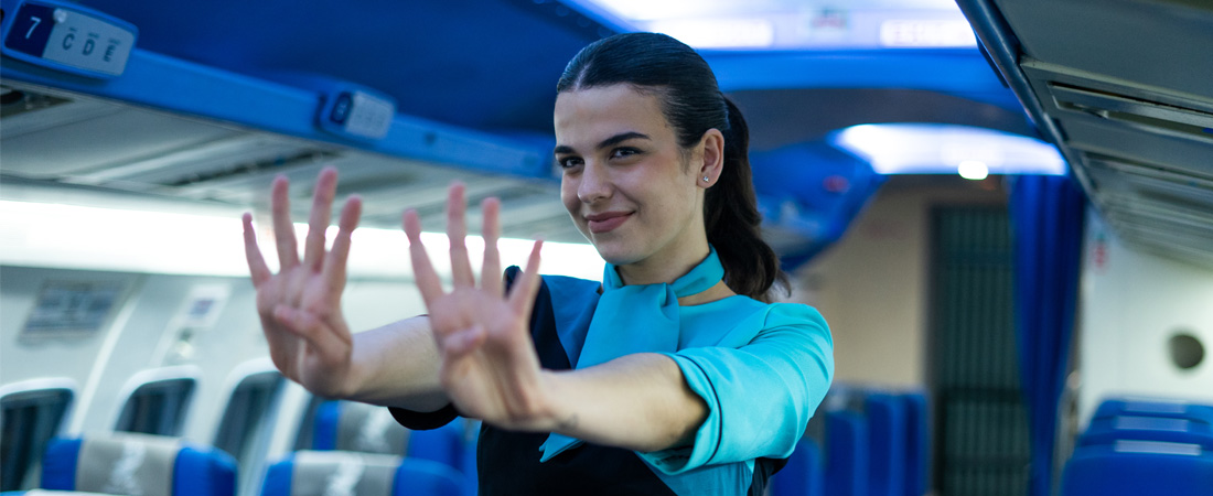 Azafata de vuelo realizando gesto de seguridad en cabina