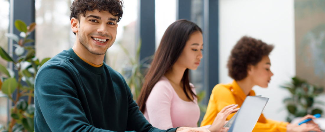Tres jóvenes sonrientes en un aula de clases prestando atención, ideal para representar el aprendizaje de idiomas para TCP.