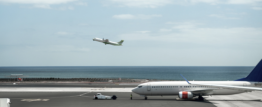 Avión comercial volando a baja altura sobre las aguas cristalinas de un mar azul bajo un cielo despejado.